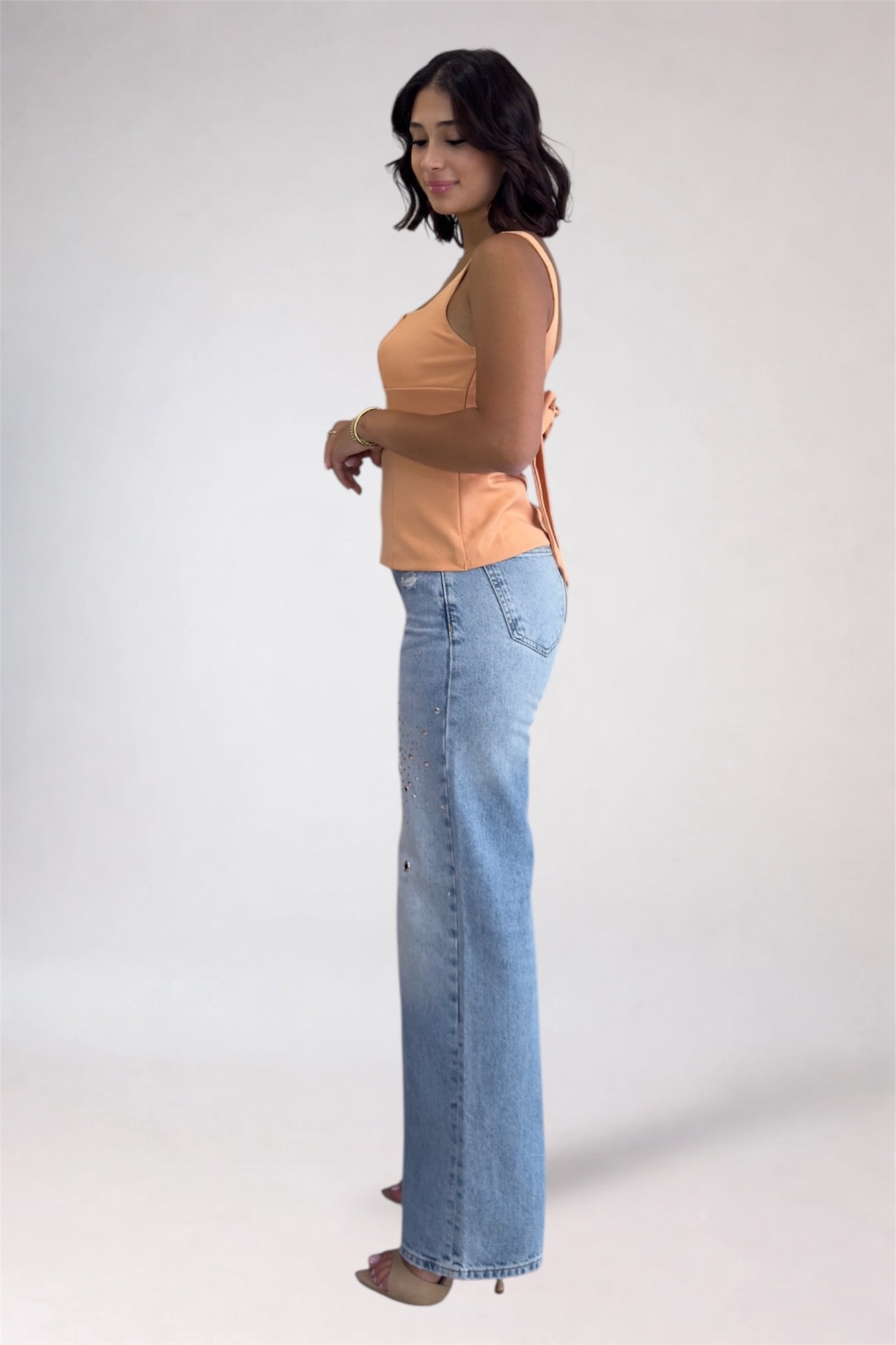 Woman wearing a peach top and light blue jeans on a white background