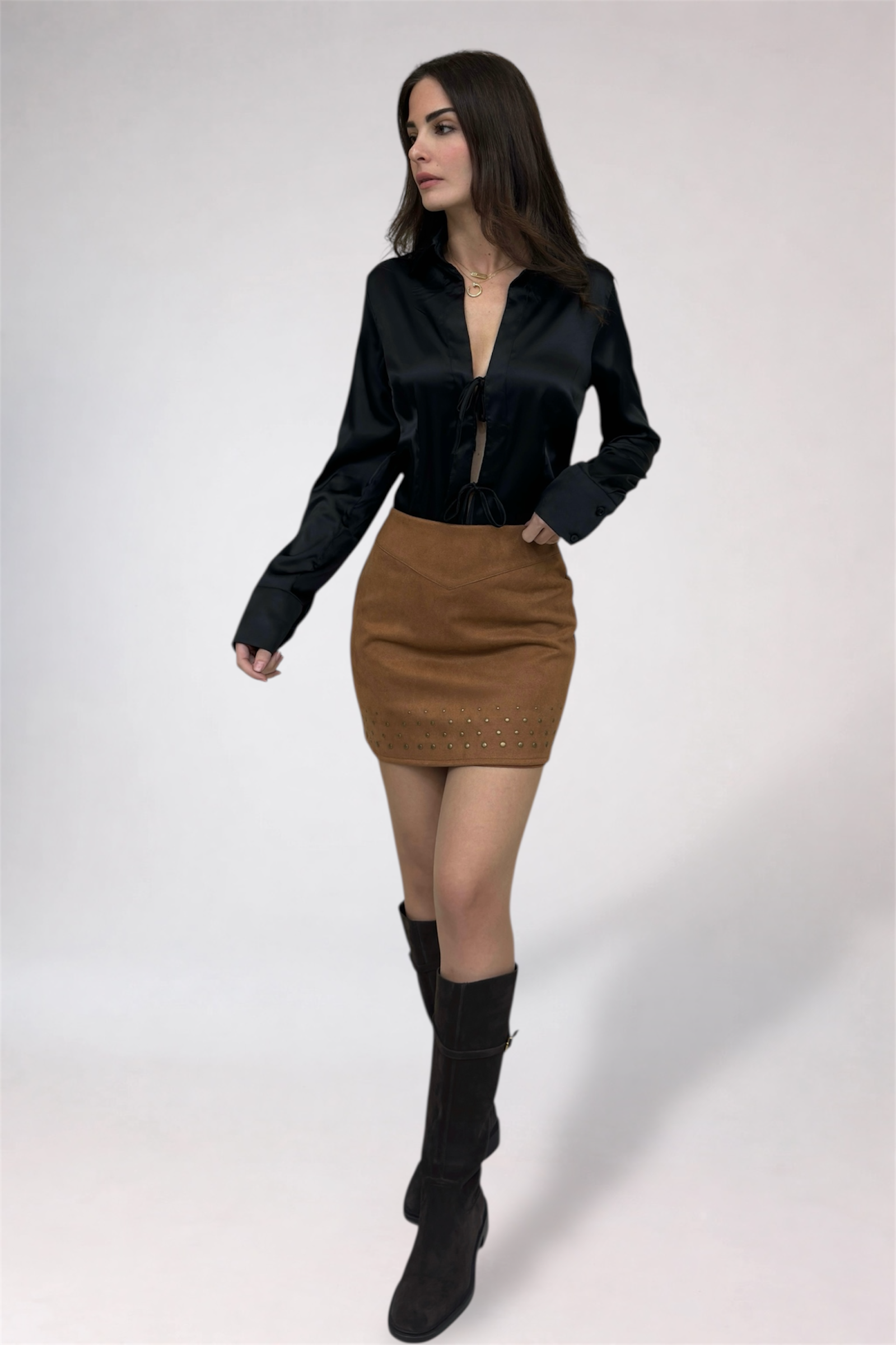 Woman wearing a black blouse, brown skirt, and black knee-high boots on a white background