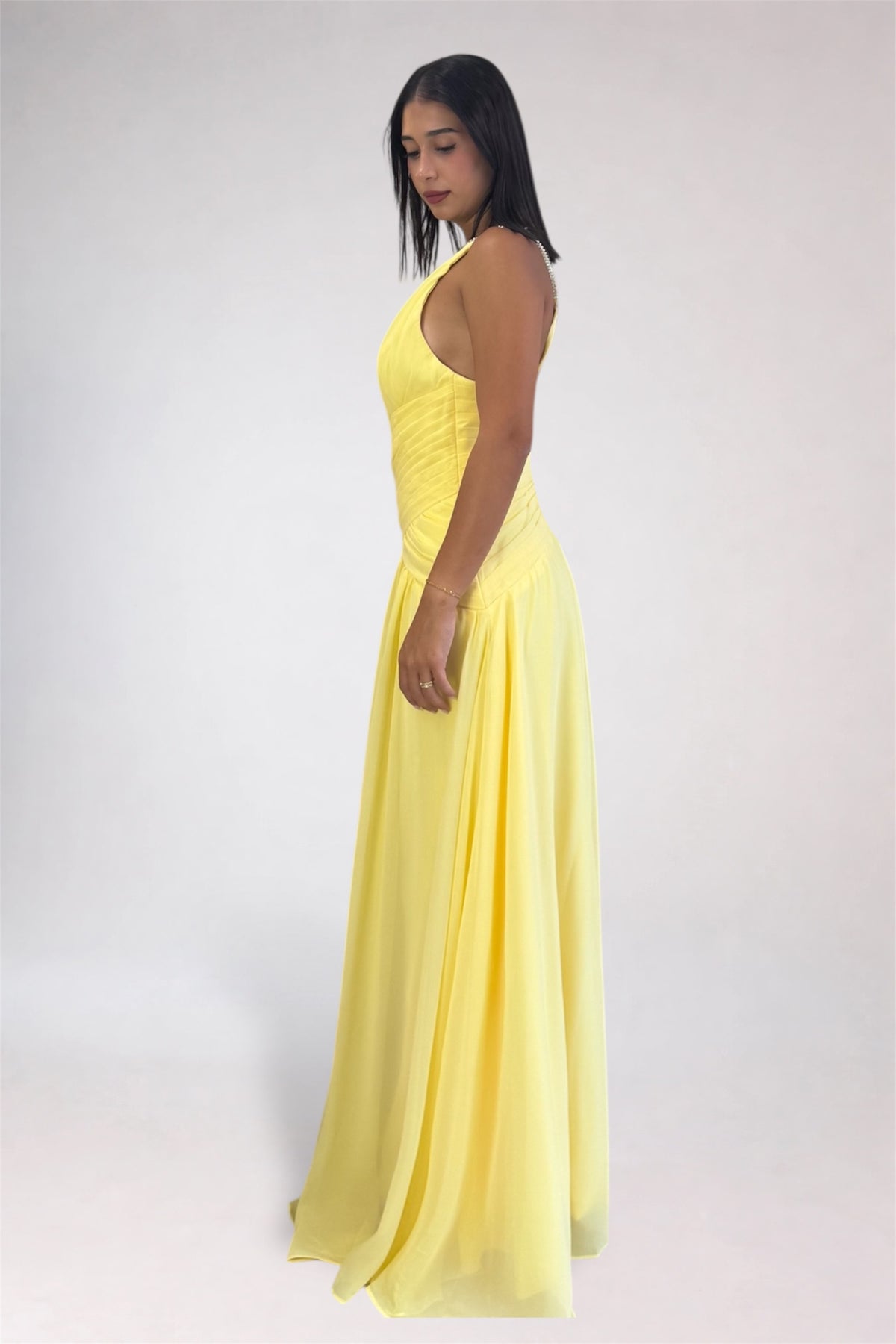 A woman modeling a sleeveless, halter-neck, floor-length yellow dress against a plain light gray studio background.