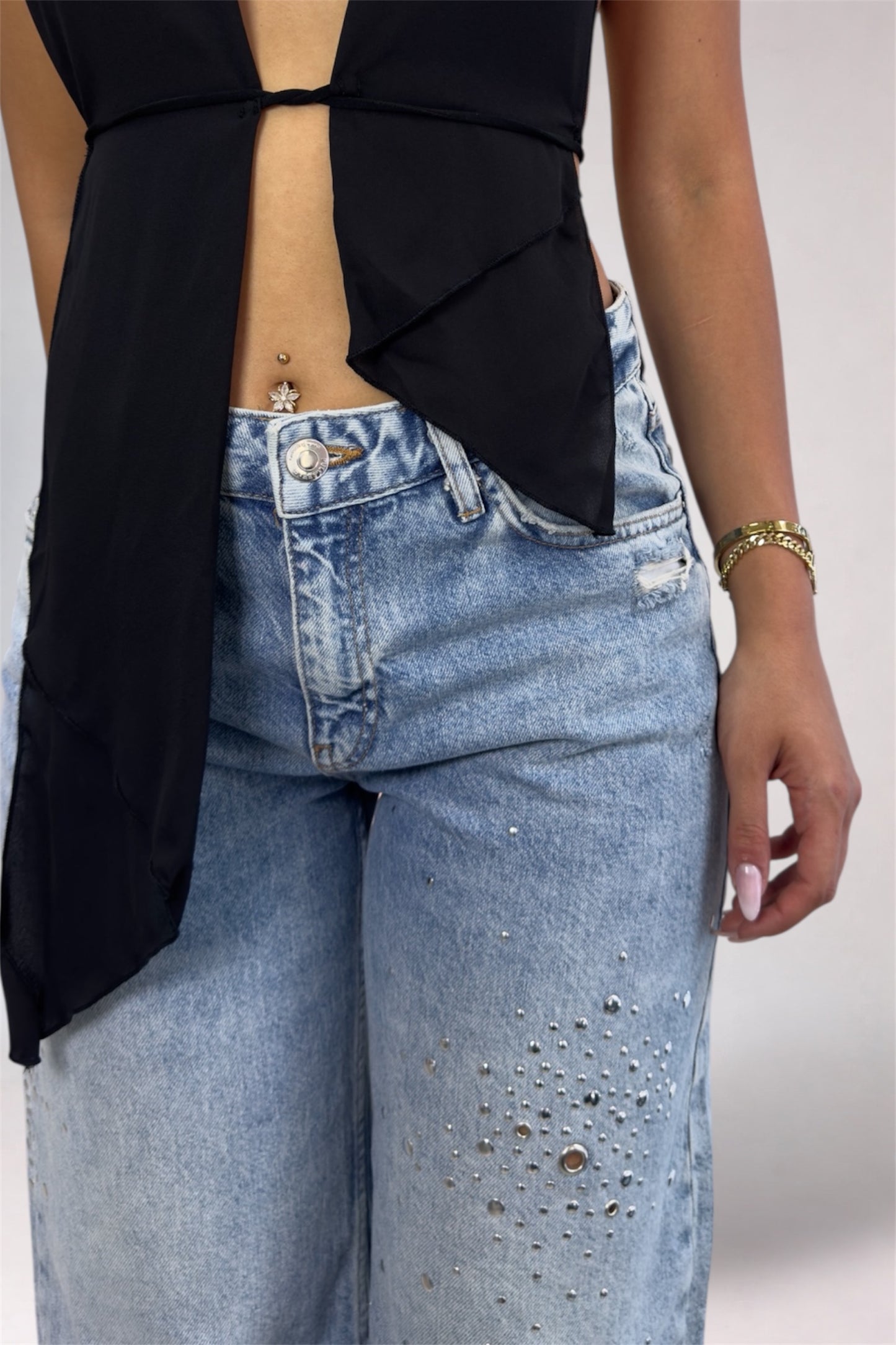 Person wearing a black top with cut-out design and blue jeans on a plain background