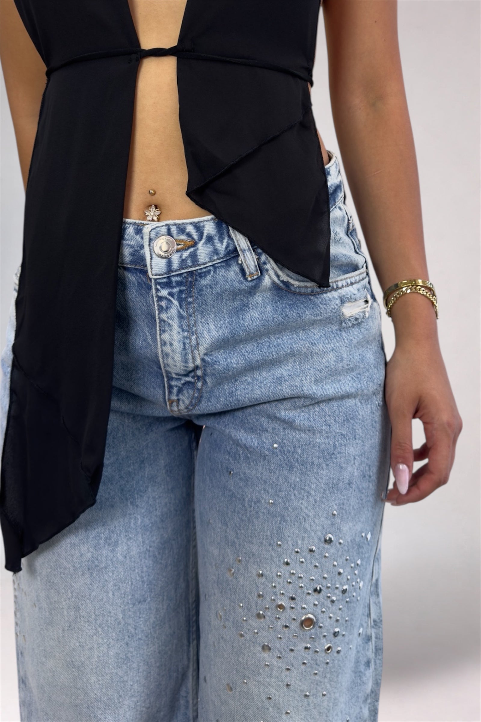 Person wearing a black top with cut-out design and blue jeans on a plain background