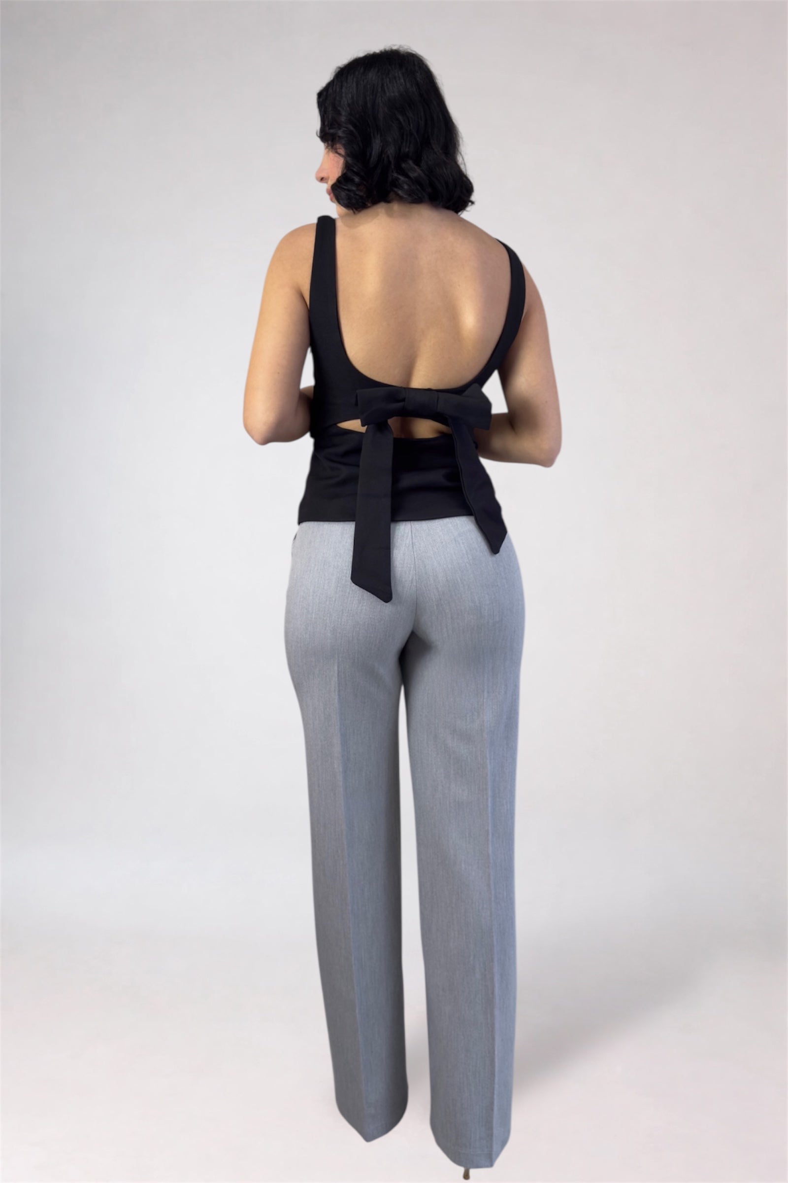 Woman wearing a black sleeveless top and gray pants on a white background