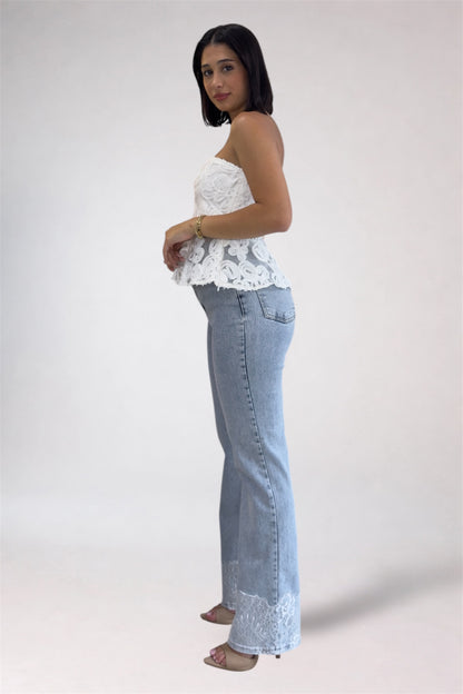 Woman wearing a white lace top and light blue jeans on a plain background