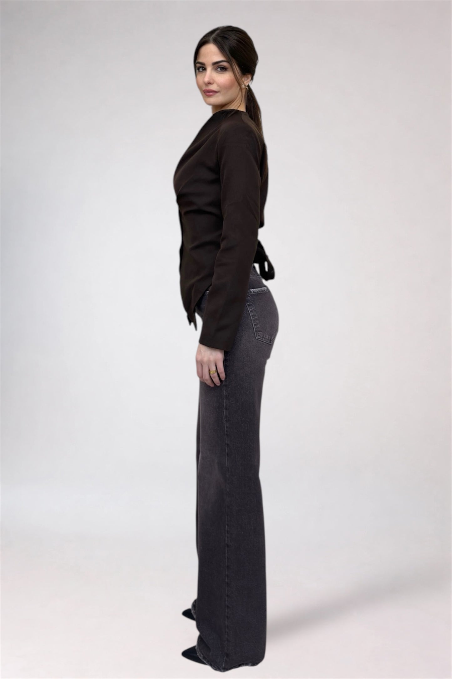 Woman wearing a black top and dark jeans on a white background