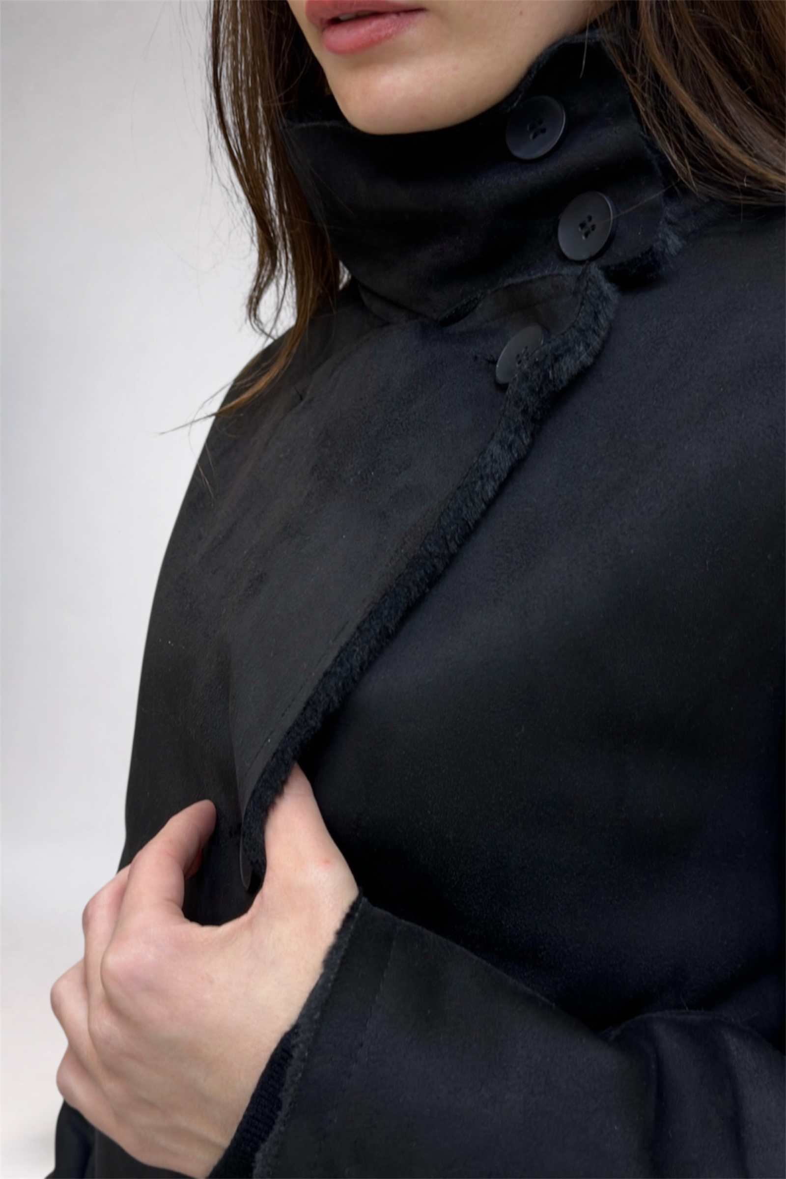 Close-up of a person wearing a black coat with a high collar on a white background