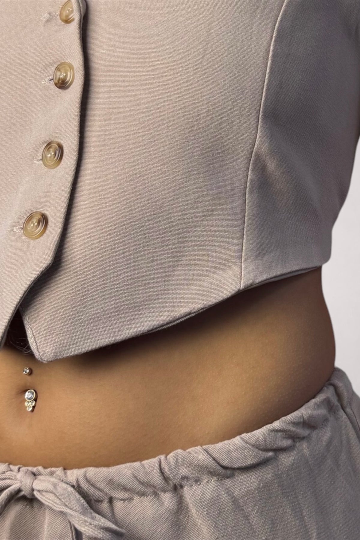 Close-up of a person wearing a light taupe cropped top with decorative buttons down the front and matching drawstring bottoms.