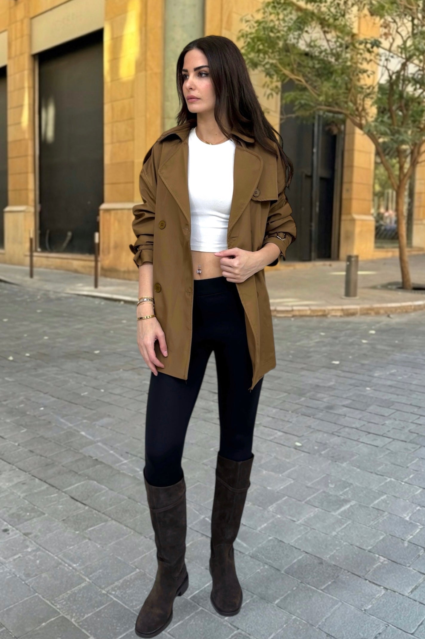 Woman wearing a brown coat, white top, black pants, and brown boots on a city street.