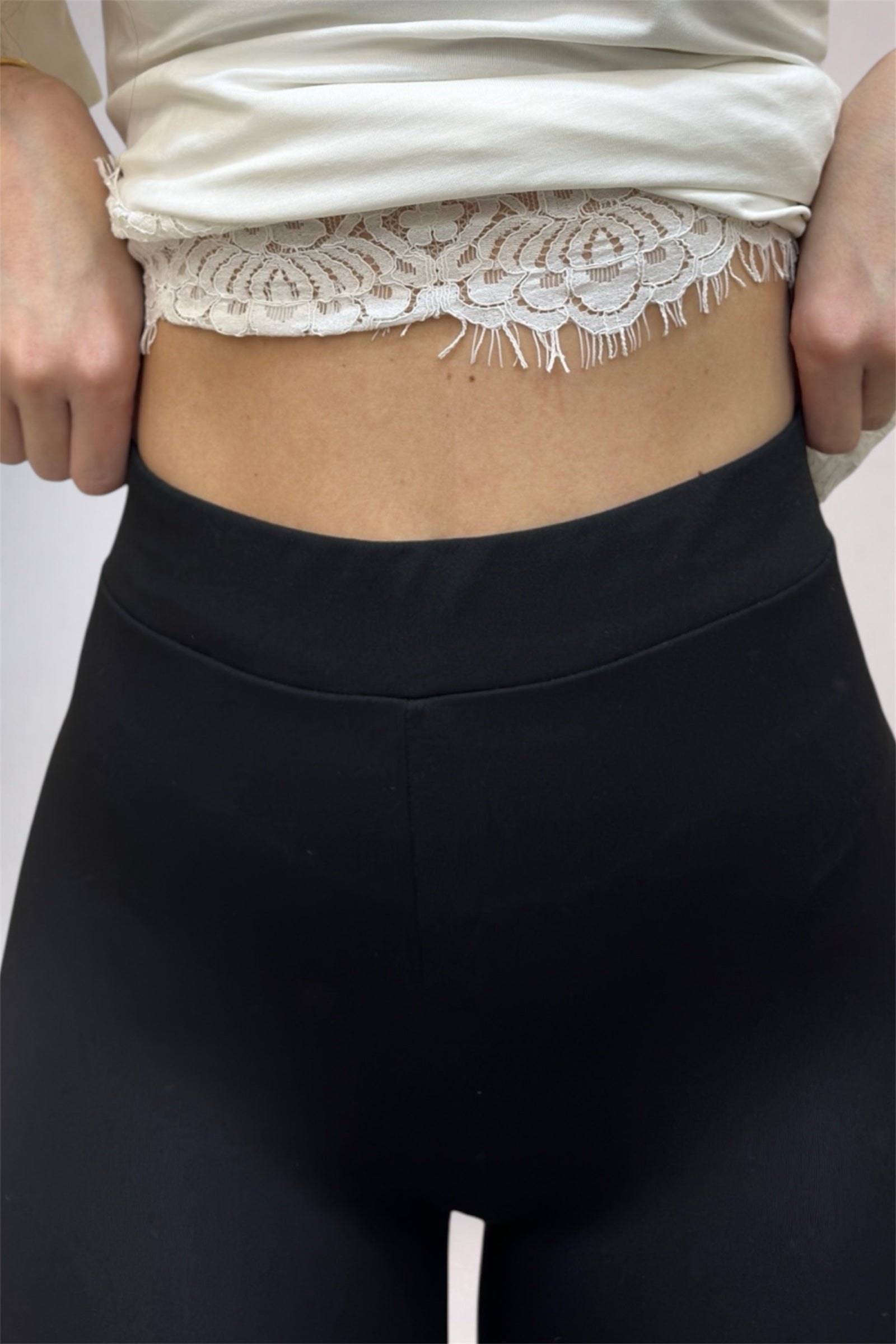Person wearing a white lace top and black pants on a plain background