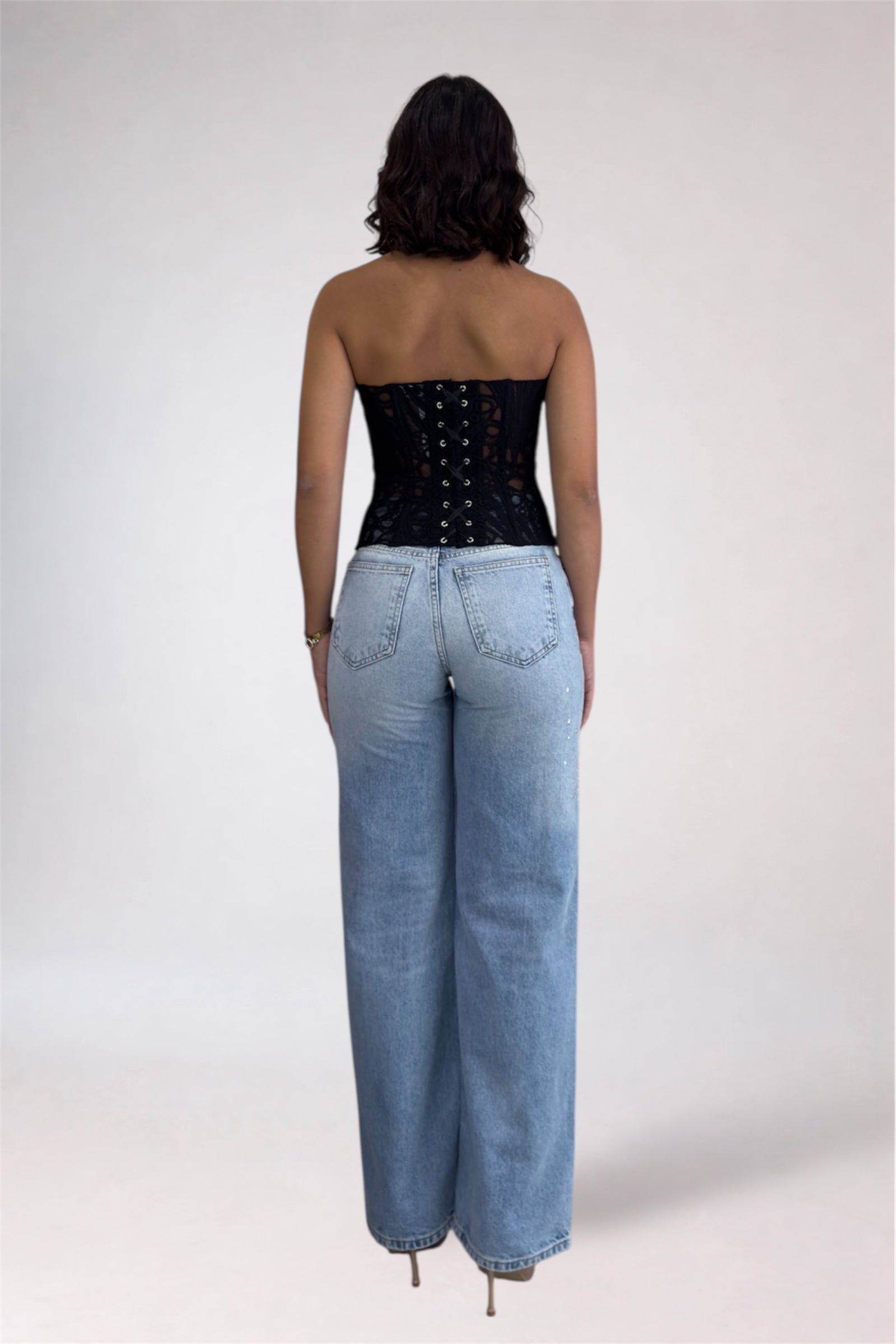 Person wearing a black strapless top and light blue jeans on a white background