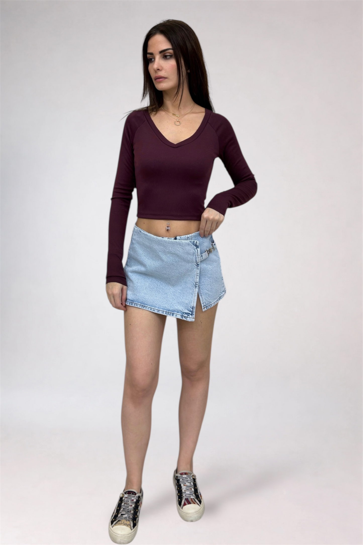 Woman wearing a burgundy long-sleeve top and light blue denim skirt on a white background