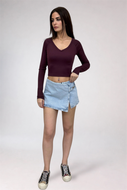 Woman wearing a burgundy long-sleeve top and light blue denim skirt on a white background