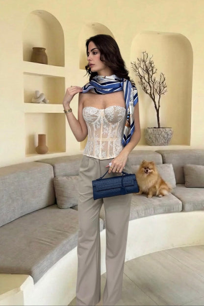 Woman in a stylish outfit with a scarf and handbag, standing in a modern living room.