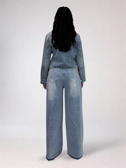 A model viewed from the back wearing a light blue denim jumpsuit with wide-leg pants and a long-sleeve top, set against a plain light gray studio background.
