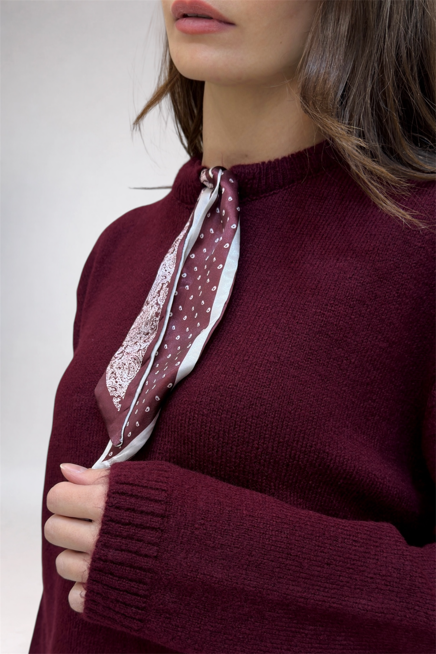 Person wearing a burgundy sweater with a matching scarf against a white background