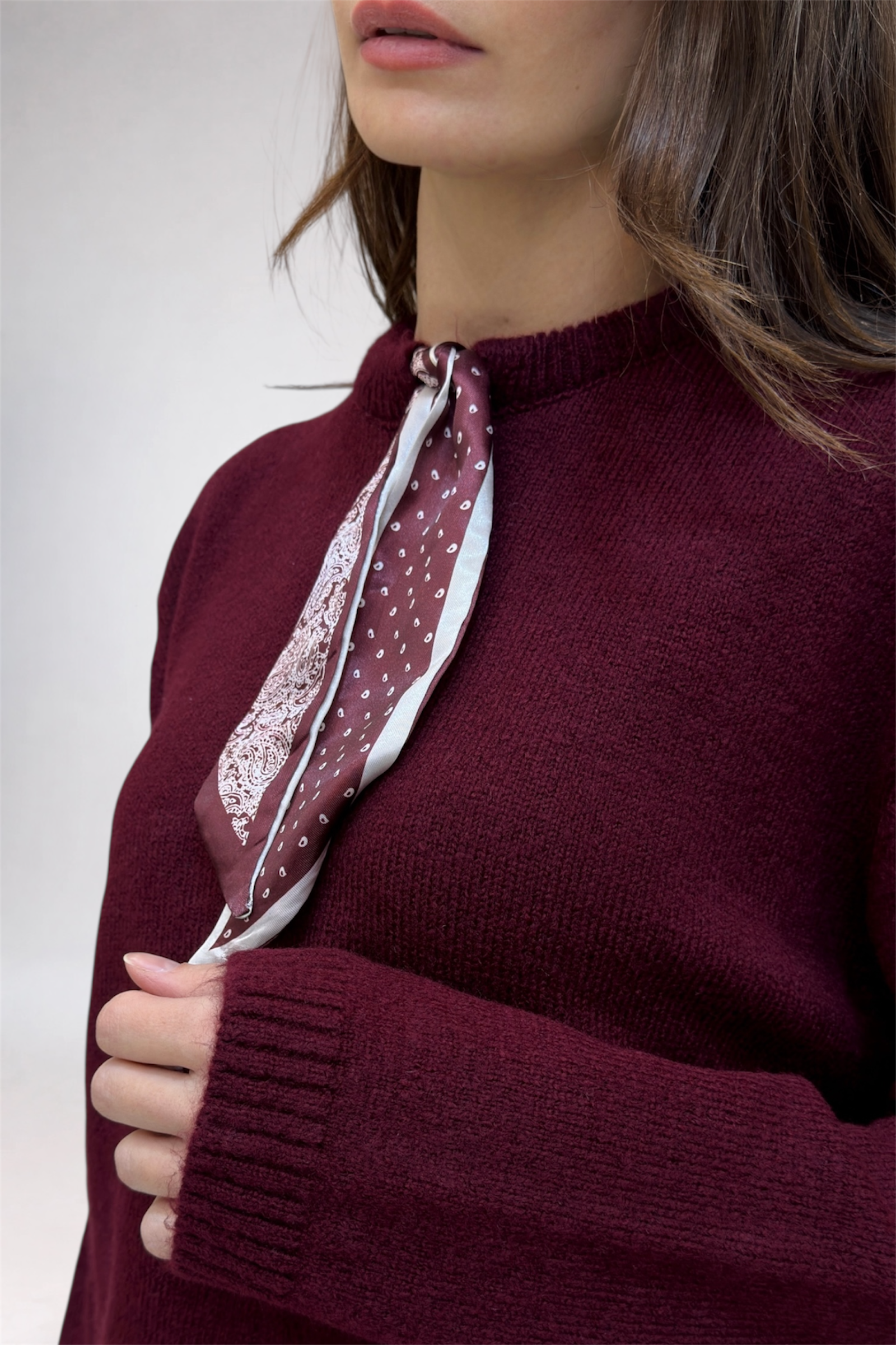 Person wearing a burgundy sweater with a matching scarf against a white background