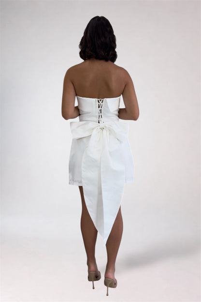 Woman wearing a white strapless dress with a bow detail on a plain background