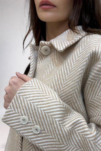 Close-up of a person wearing a herringbone patterned coat with a neutral background