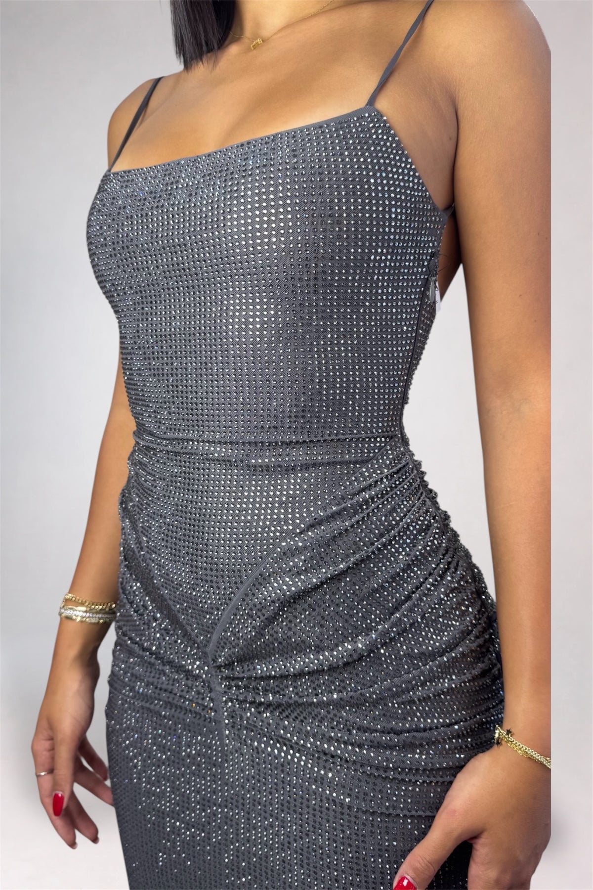 A woman wearing a shimmering silver backless maxi dress and beige high heels, standing on a studio background