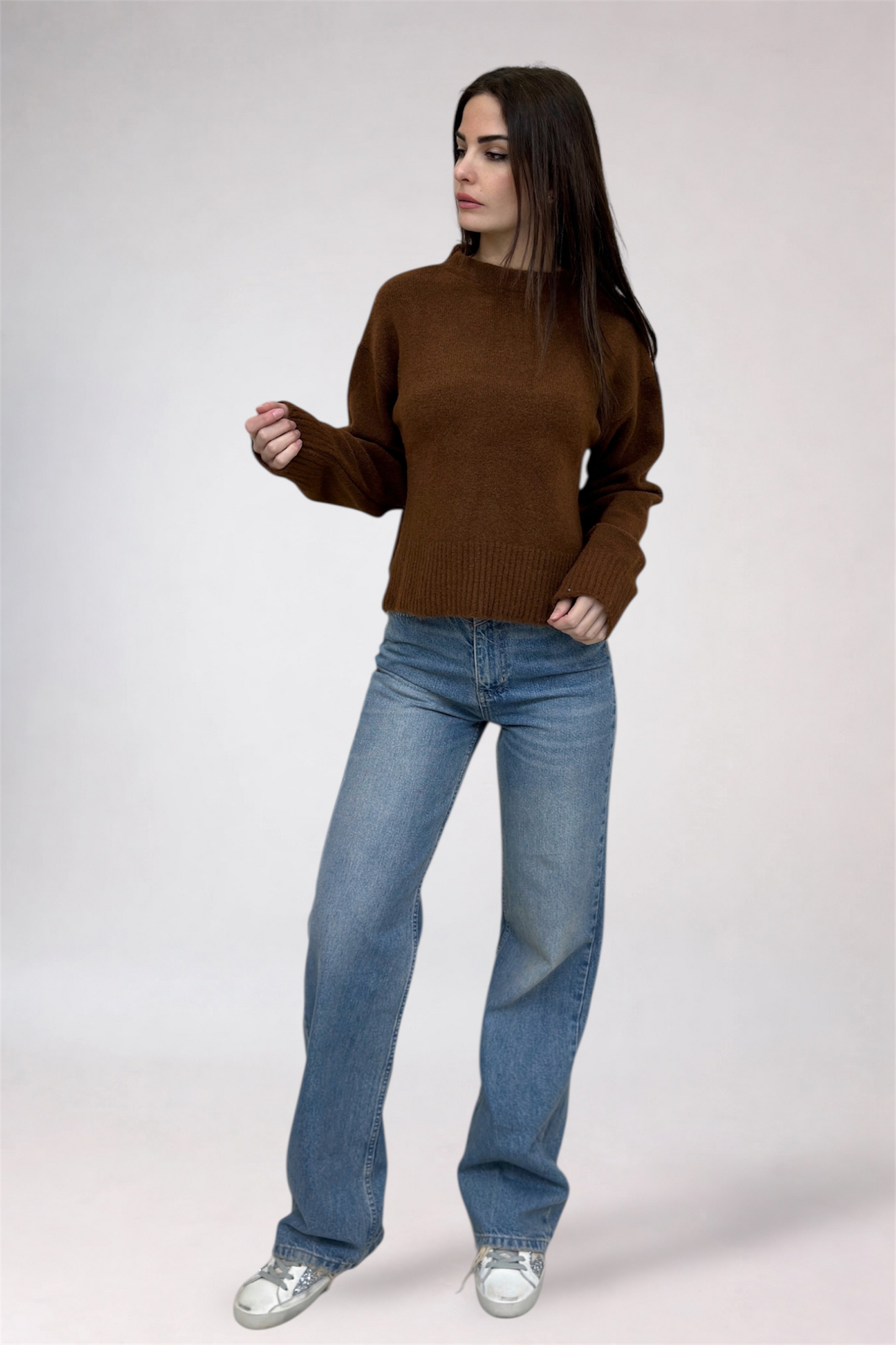 Woman wearing a brown sweater and blue jeans on a white background