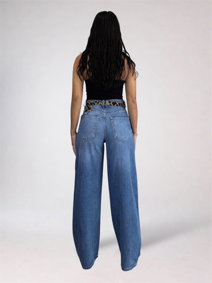 A woman shown from the back wearing wide-leg blue jeans with a leopard-print belt, a black sleeveless top, and light skin against a plain light gray studio background.