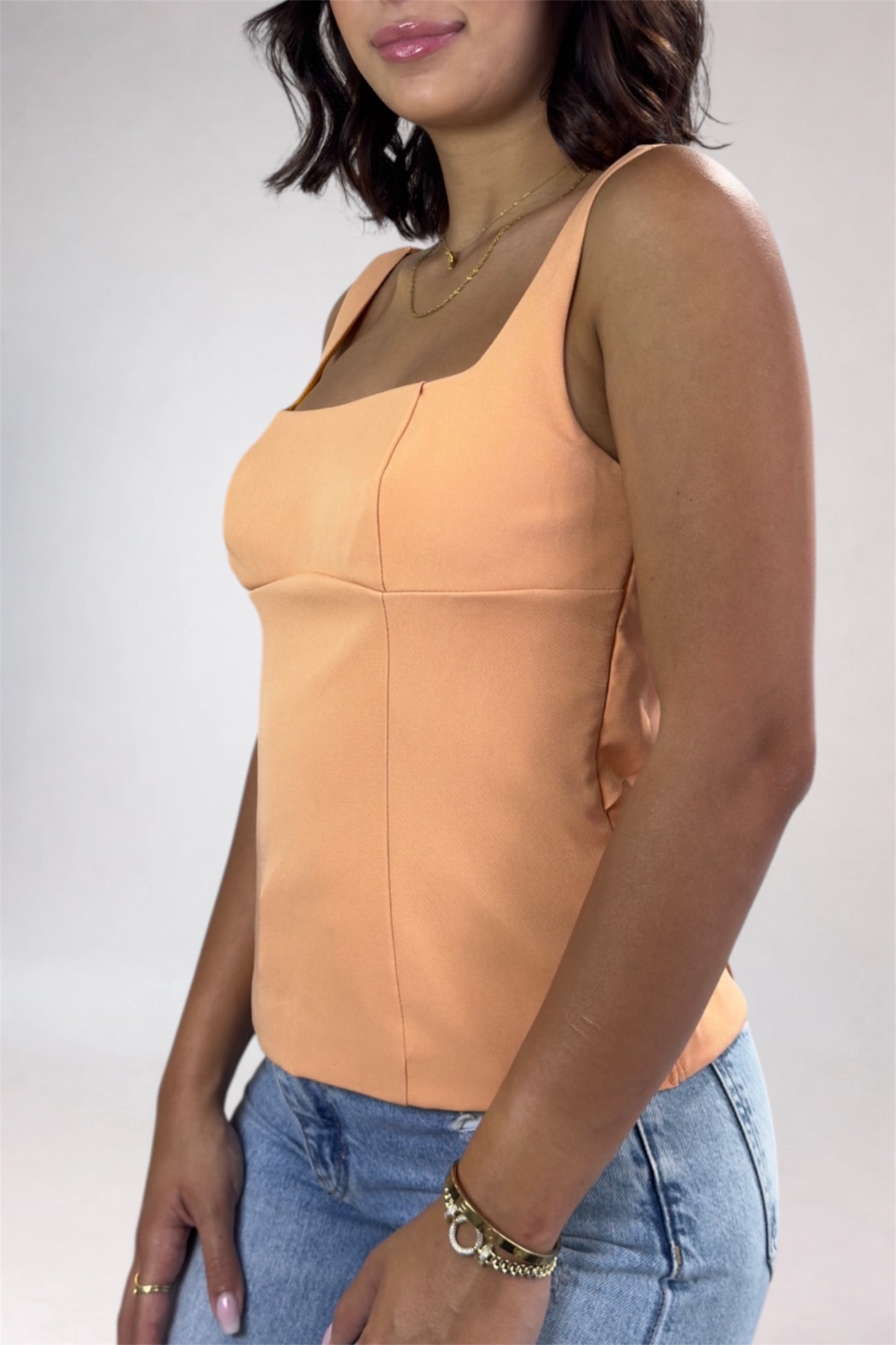 Woman wearing a peach tank top and blue jeans against a plain background
