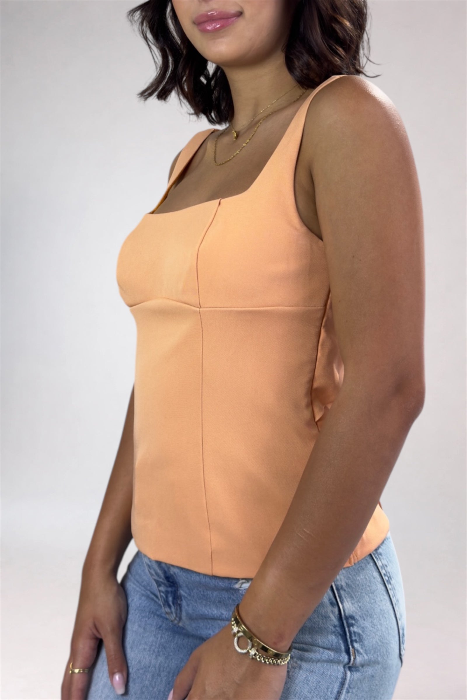 Woman wearing a peach tank top and blue jeans against a plain background
