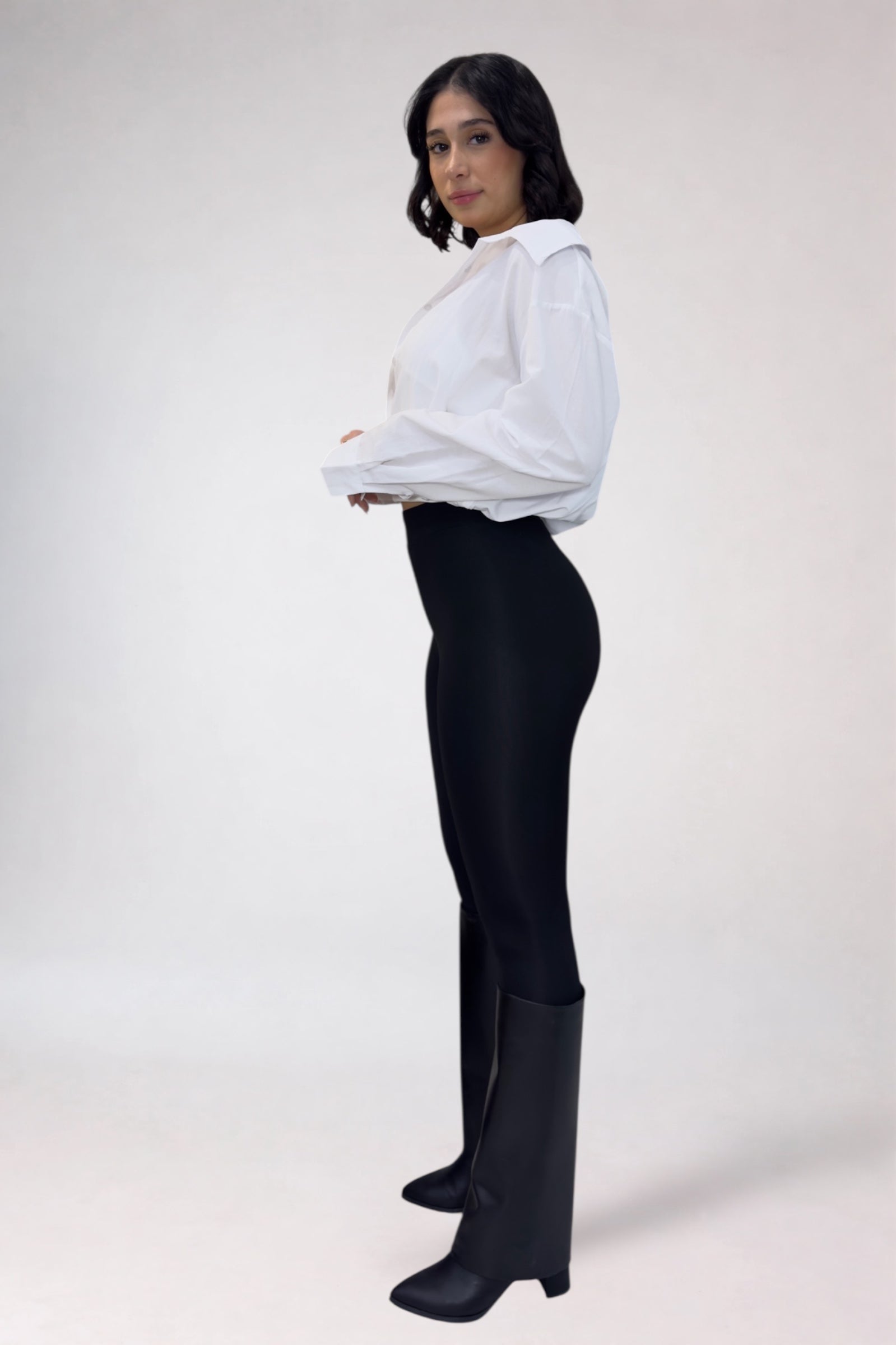 Person wearing a white blouse and black pants with black boots on a white background