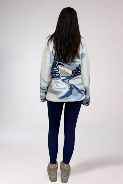 Person wearing a patterned sweater with a scenic design on a plain background