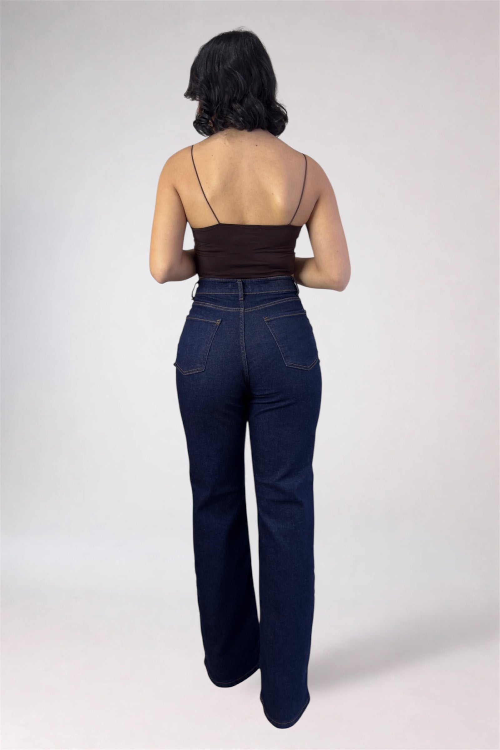 Woman wearing dark blue jeans and a brown top on a white background