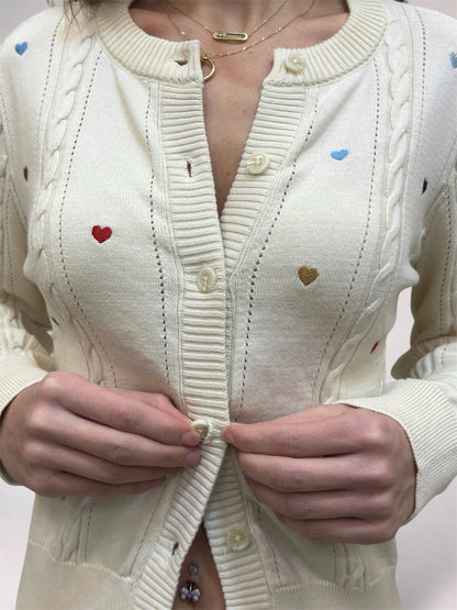 Close-up of a person wearing a cream-colored sweater with heart patterns, focusing on the chest area.