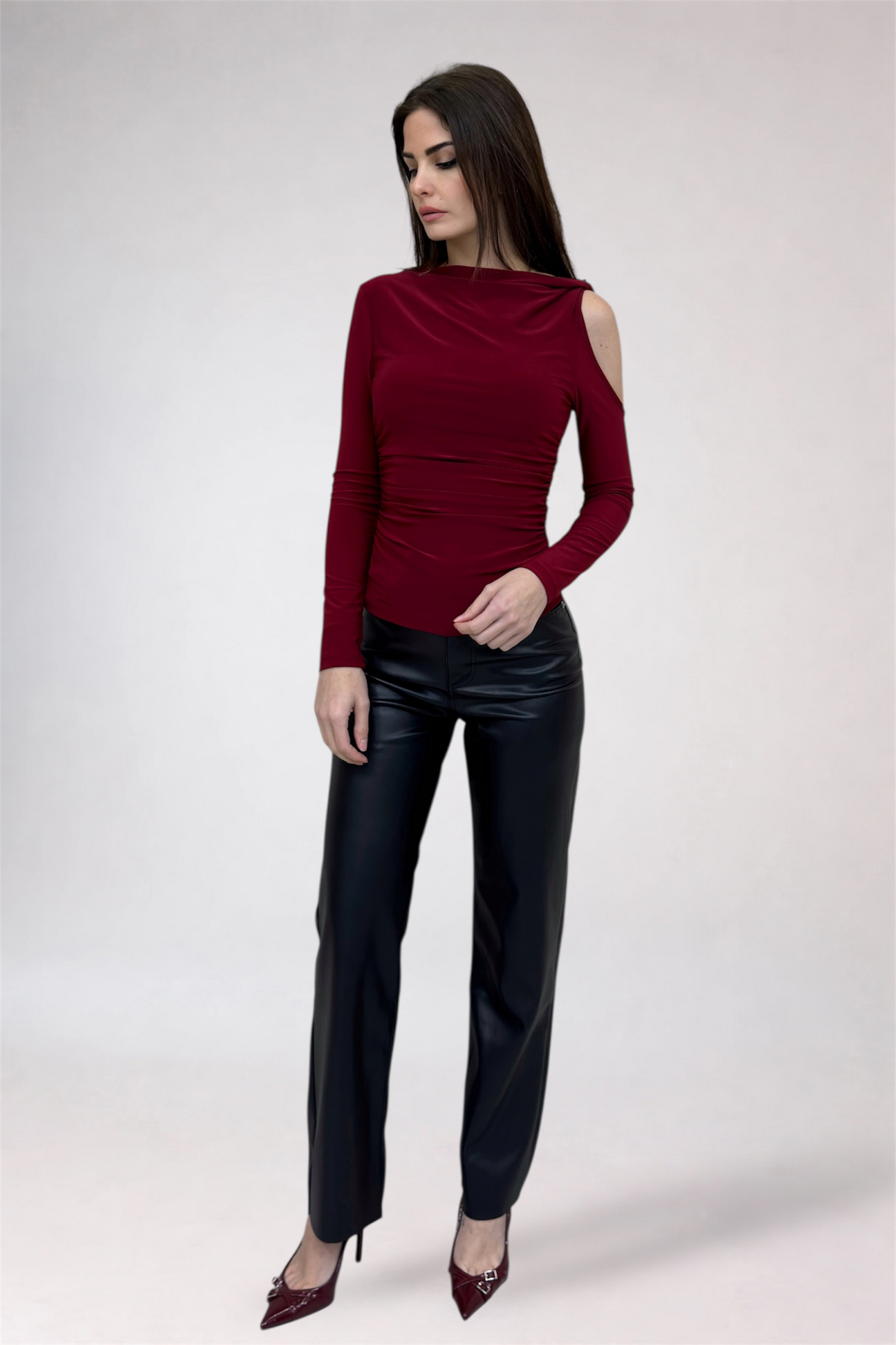 Woman wearing a burgundy long-sleeve top and black leather pants on a white background
