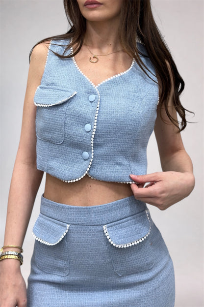 Woman wearing a light blue outfit with a matching vest and skirt against a neutral background