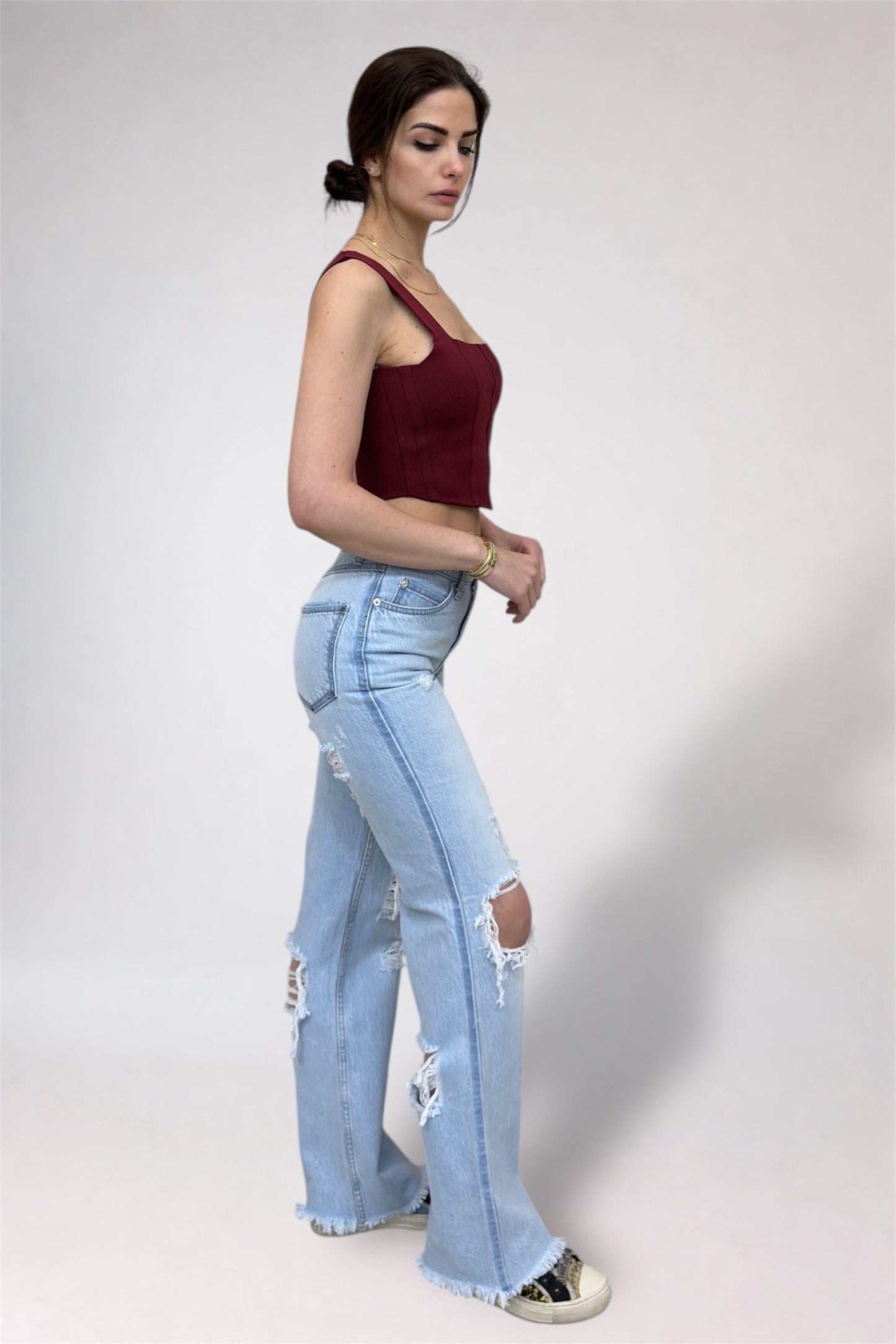 Woman wearing a burgundy top and light blue jeans on a white background