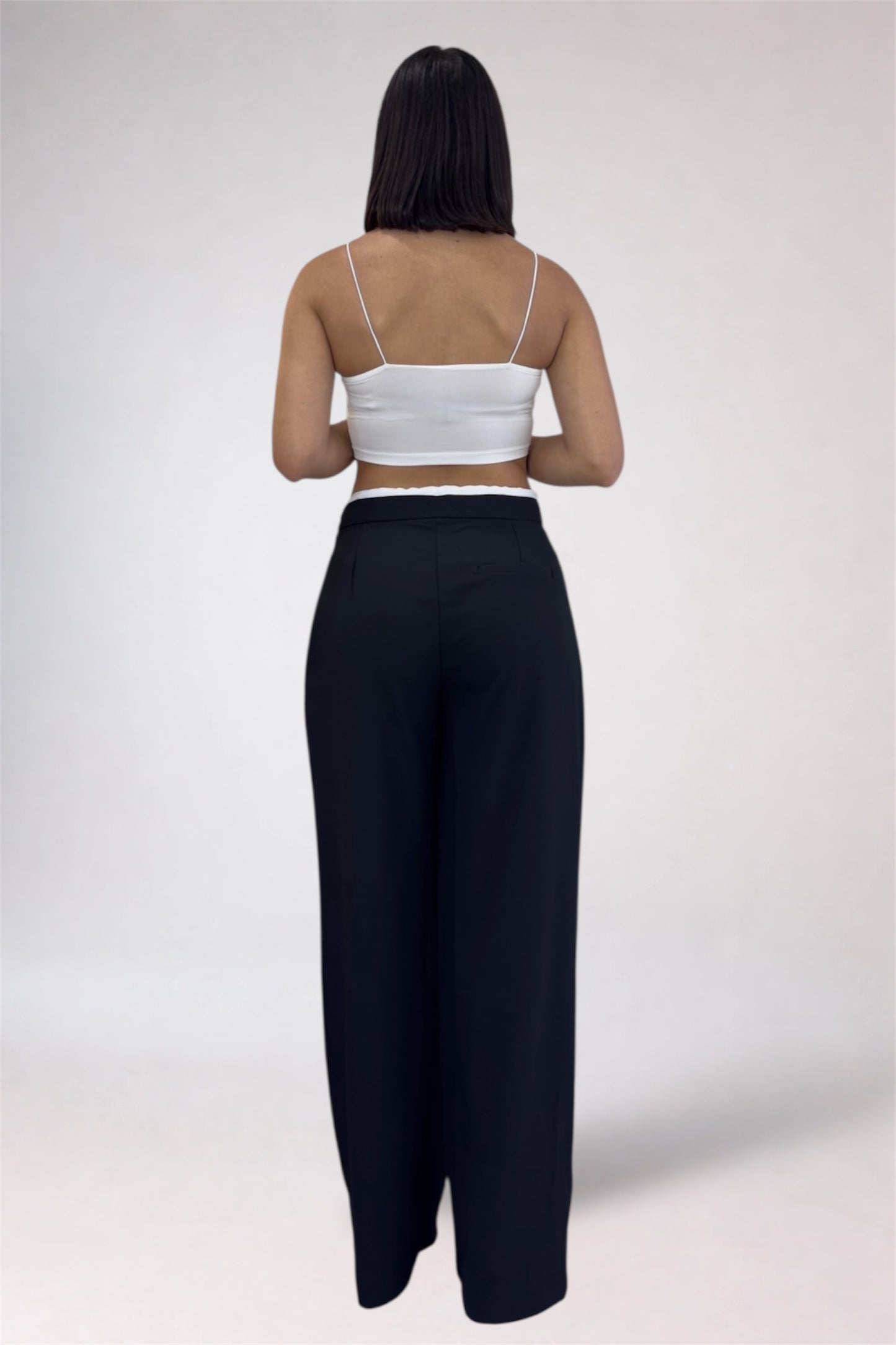 Person wearing a white top and black pants on a plain background