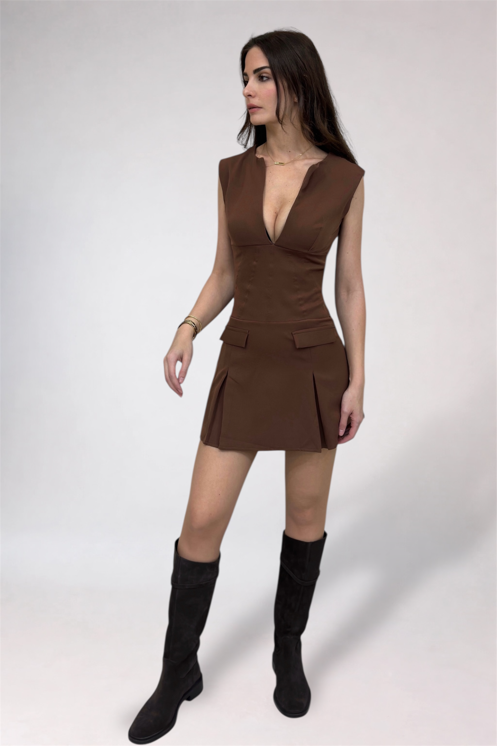 Woman wearing a brown dress with a plunging neckline and black knee-high boots on a white background