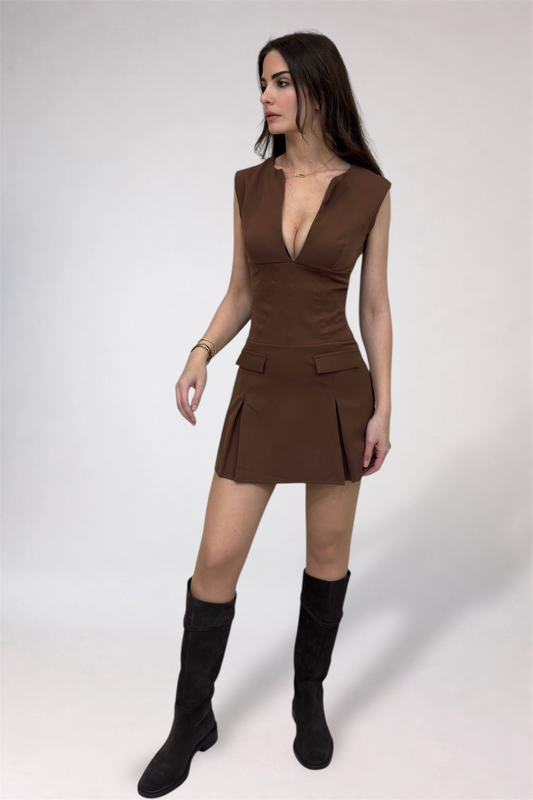 Woman wearing a brown dress with a plunging neckline and black knee-high boots on a white background