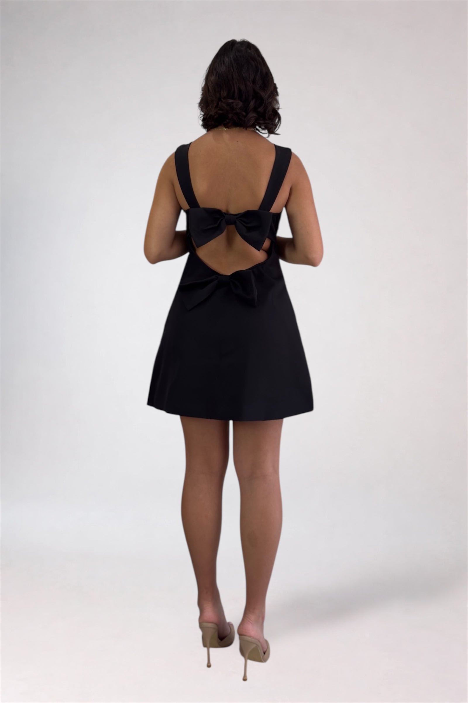 Black dress with a bow detail on the back worn by a person on a white background