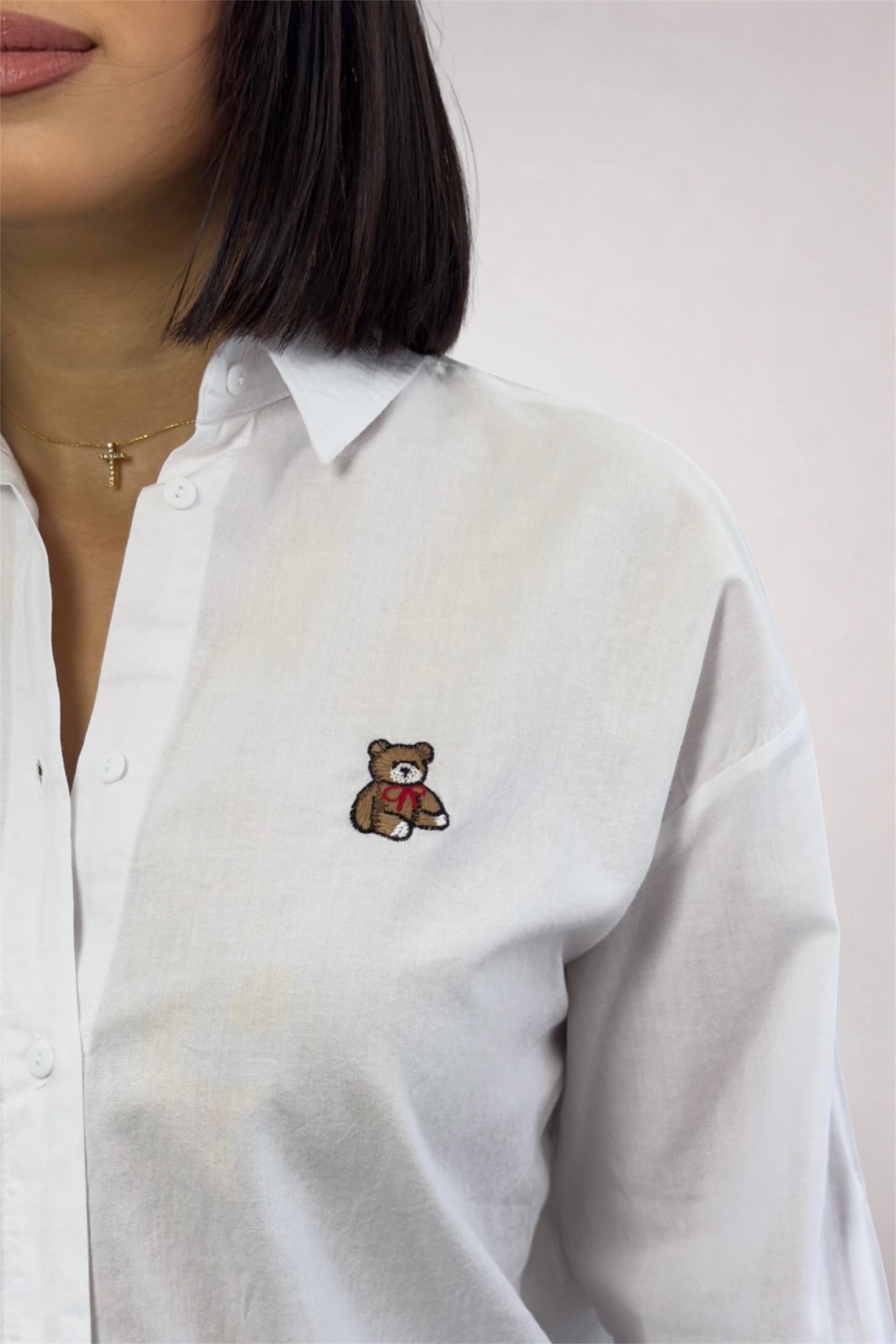 White shirt with a teddy bear embroidery detail on a plain background