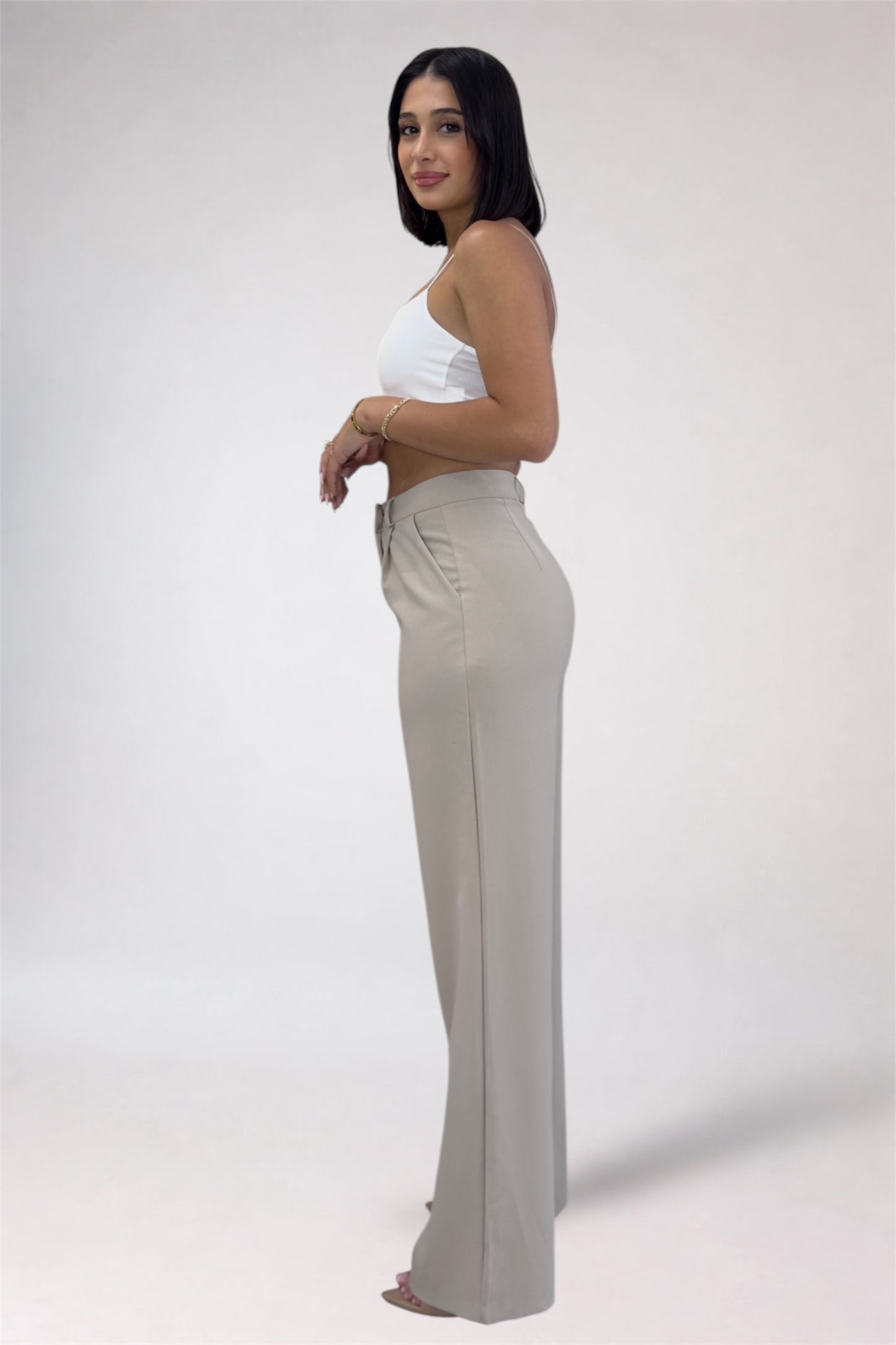 Woman wearing a white top and beige flared pants on a plain background