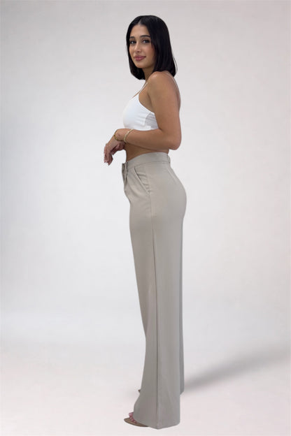Woman wearing a white top and beige flared pants on a plain background