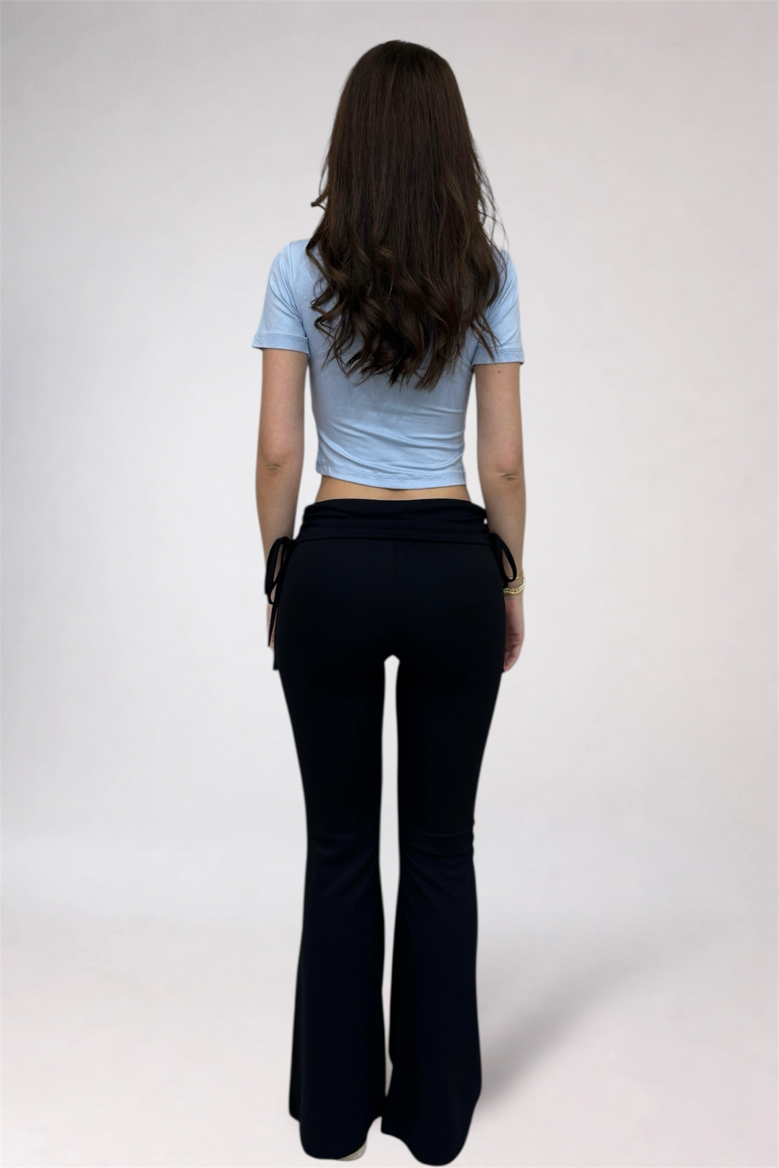 Person wearing a light blue crop top and black flared pants on a white background