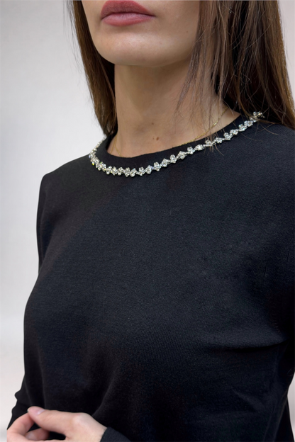 Person wearing a black top with a decorative necklace against a white background