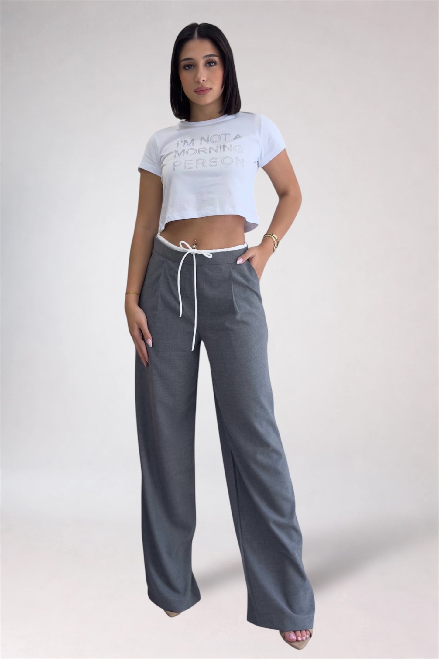 Woman wearing a white crop top and gray wide-leg pants on a plain background