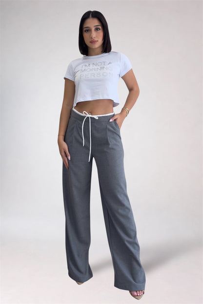 Woman wearing a white crop top and gray wide-leg pants on a plain background