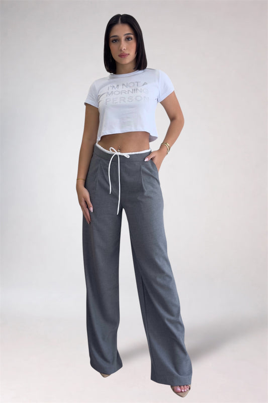 Woman wearing a white crop top and gray wide-leg pants on a plain background