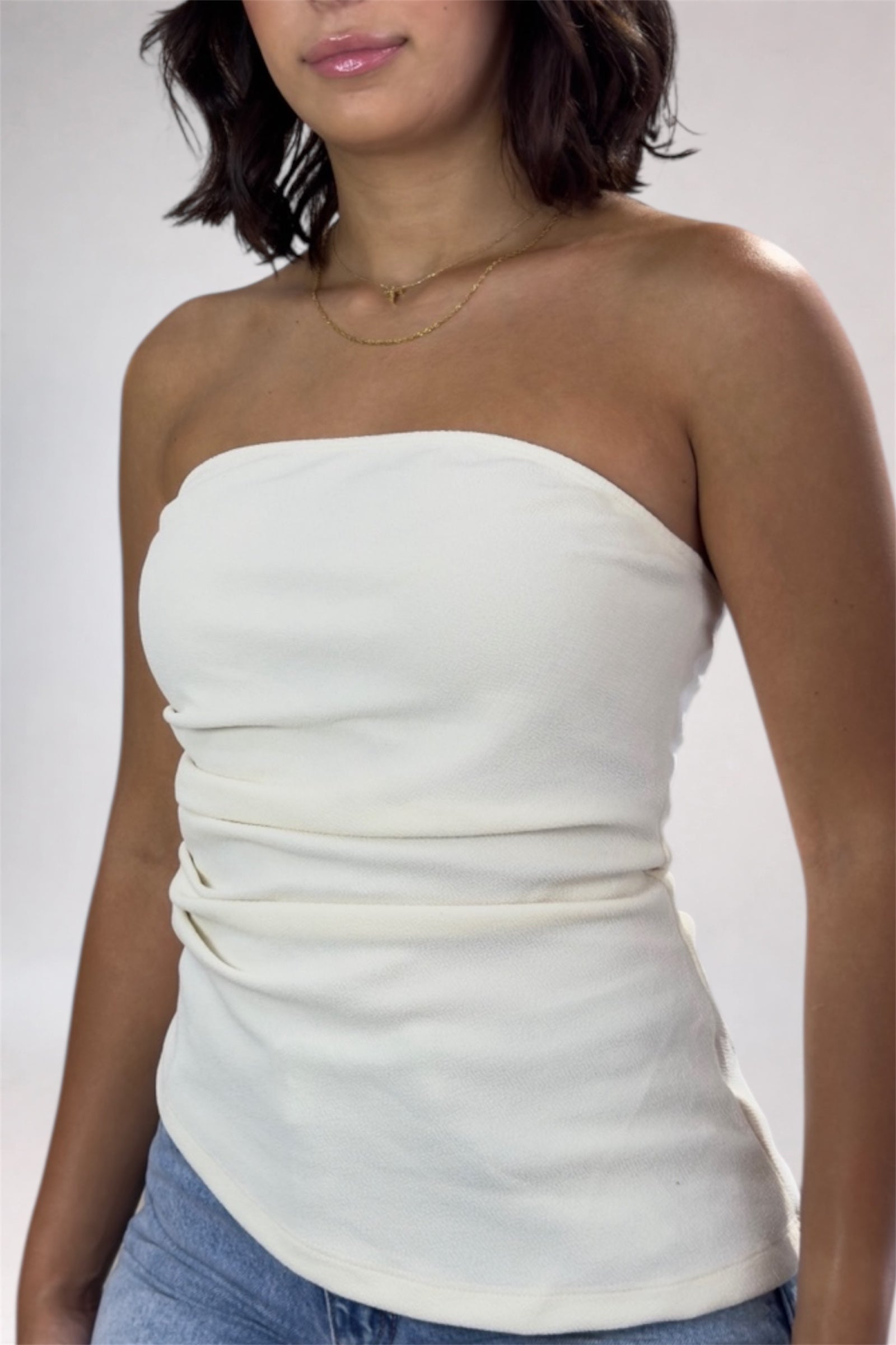 Woman wearing a white strapless top and blue jeans against a plain background