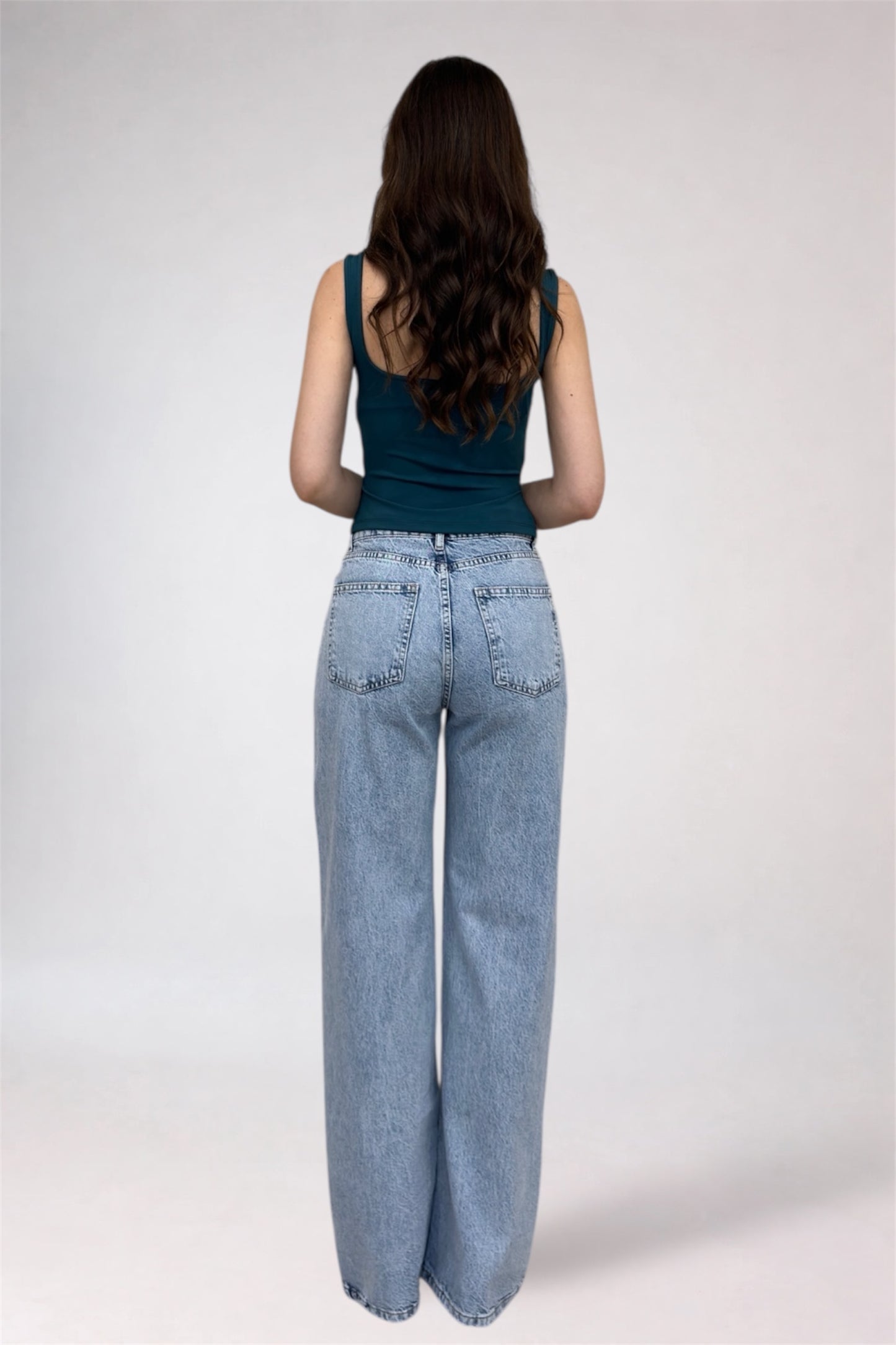Person wearing light blue jeans and a dark green top on a white background