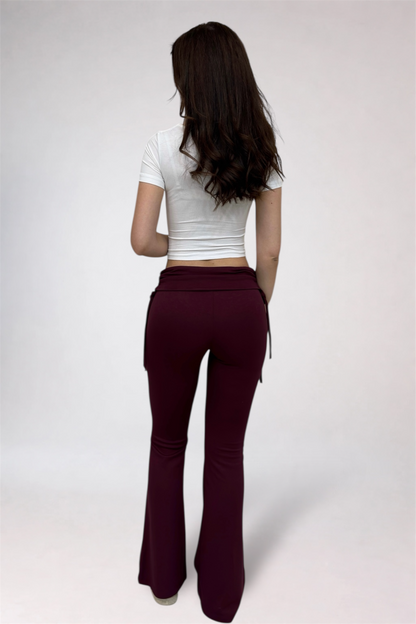 Woman wearing a white crop top and burgundy flared pants on a plain background