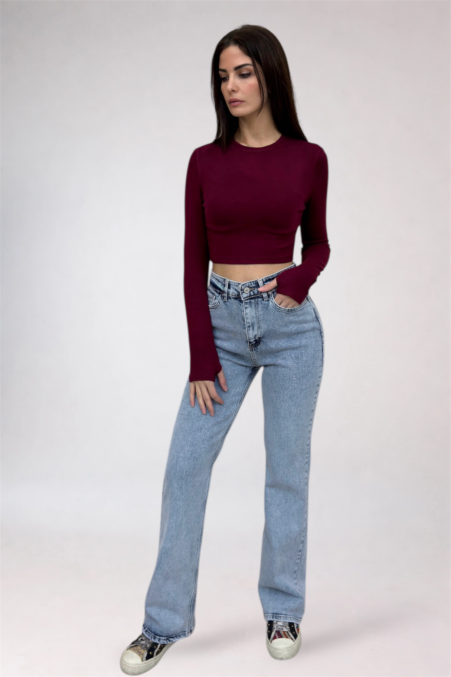 Woman wearing a burgundy long-sleeve top and light blue jeans on a white background