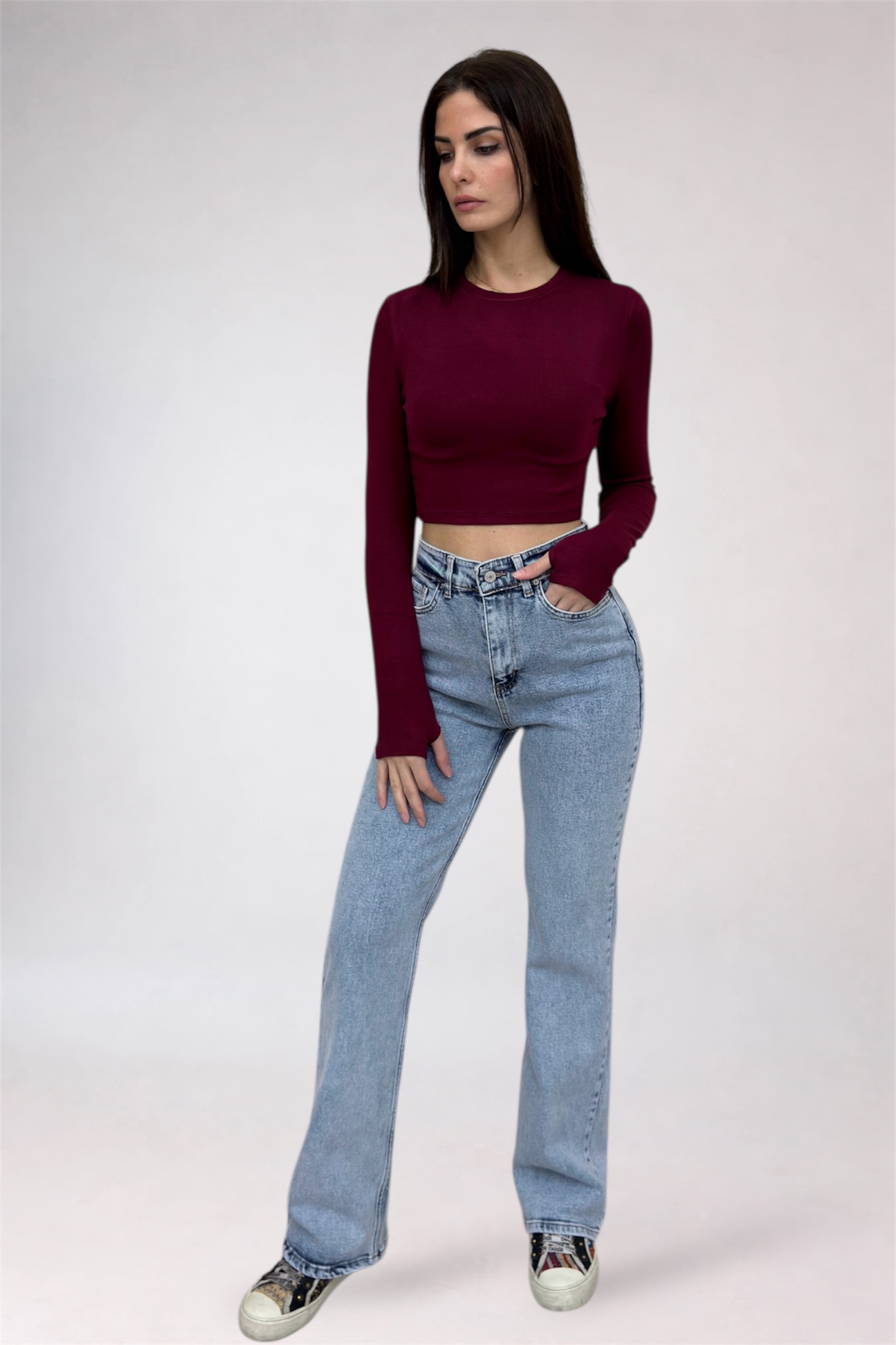 Woman wearing a burgundy long-sleeve top and light blue jeans on a white background